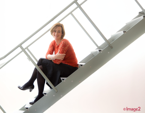 A smiling woman sits on metal stairs.
