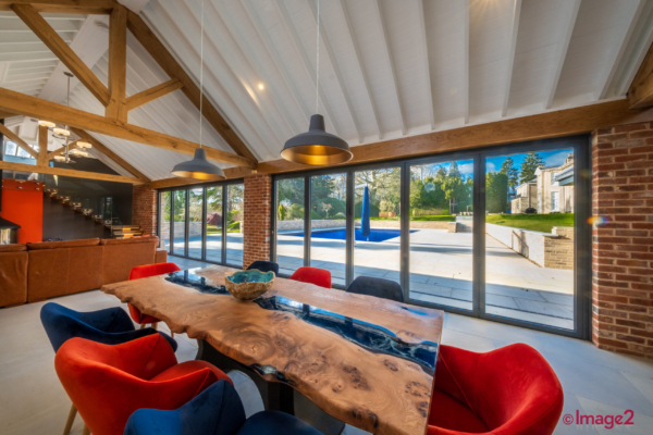 Bright dining room with exposed wood beams, a live-edge table with blue resin, and glass doors opening to a pool.
