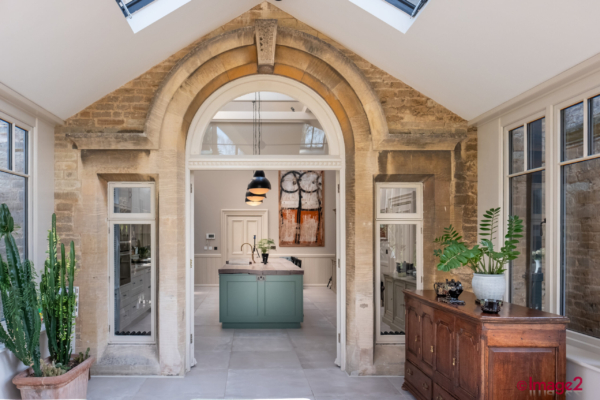 Elegant stone archway opening into a bright kitchen with a green island, under a vaulted skylight ceiling.