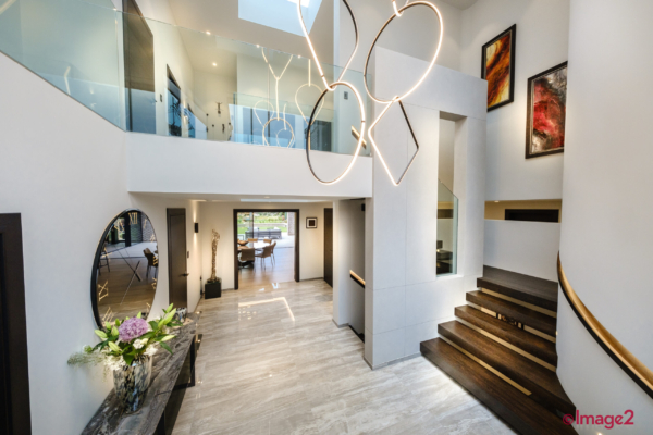 Modern hall with a high ceiling, unique ring light fixture, glass balcony, and wooden stairs.