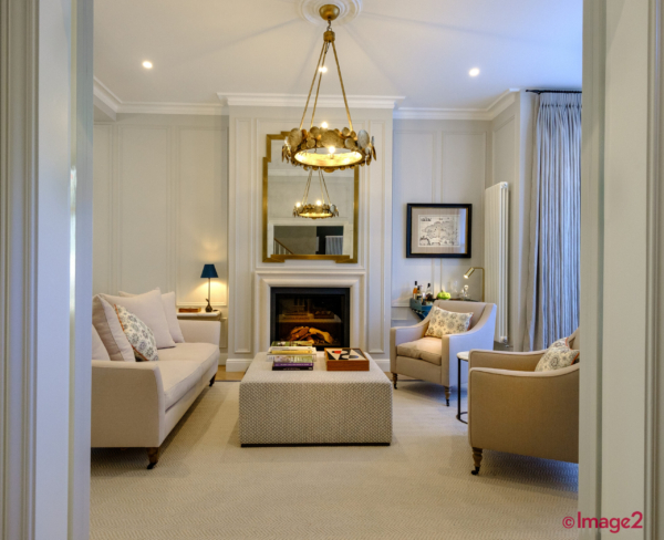 Elegant living room with beige sofas, a fireplace with a gold mirror, and a tiered chandelier.