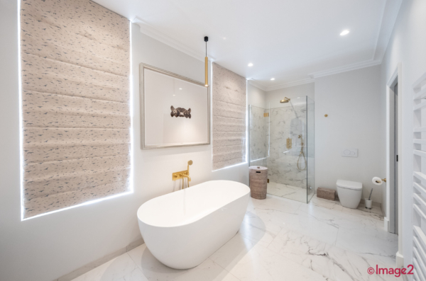 Minimalist bathroom featuring a freestanding tub, gold fixtures, marble floors, and a glass-enclosed shower.