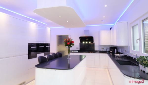 Modern white kitchen with a dark central island, sleek integrated appliances, and blue LED accent lighting.