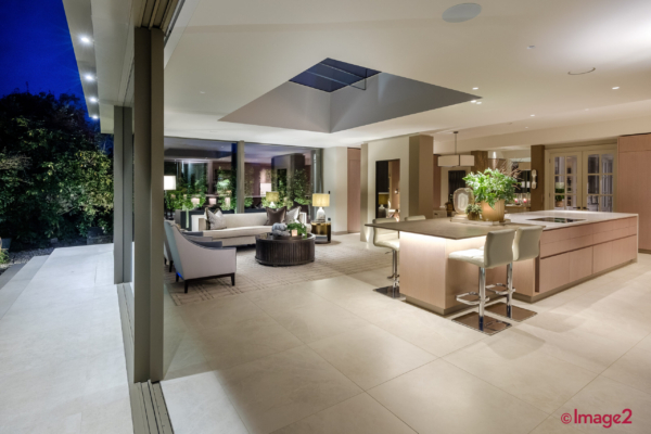Luxurious open plan kitchen and living area with a large island, glass walls, and a skylight at night.