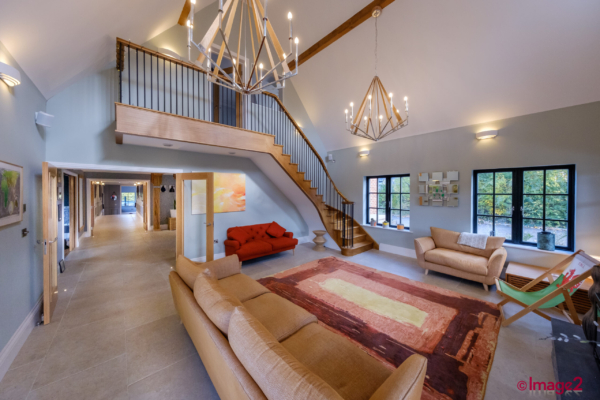 Open-plan home interior with a wooden staircase, glass balcony, and comfortable sofas.