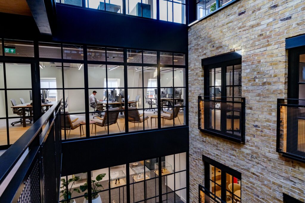 Modern multi-level office atrium with large grid windows, black steel framing, and a brick wall facade.