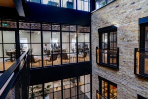 Modern multi-level office atrium with large grid windows, black steel framing, and a brick wall facade.