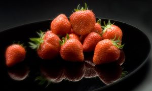 Fresh, bright red strawberries piled on a reflective black surface against a dark background