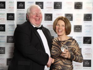 Man and woman smiling at an awards event; woman holds a small crystal globe trophy.