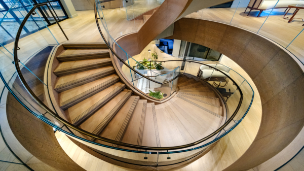 High-angle view of a dramatic, spiral wooden staircase with glass railings in a modern building.