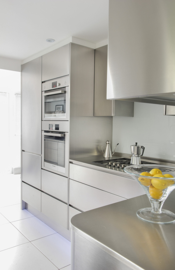 Sleek, minimalist kitchen featuring seamless stainless steel cabinets, integrated ovens, and a bowl of lemons.