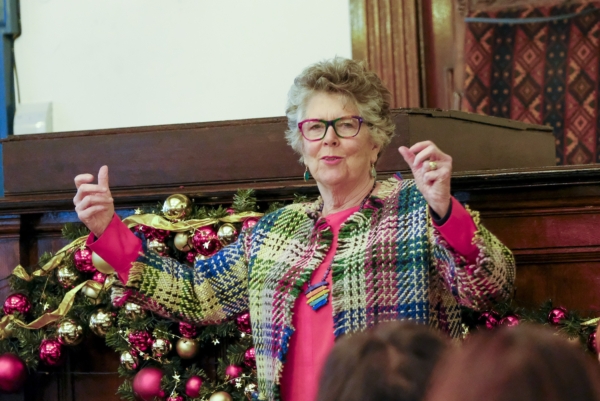 Prue Leith in a colourful patterned jacket gestures expressively while speaking in front of Christmas decorations .