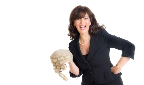 A laughing woman in a black suit holds a traditional legal wig against a white background.