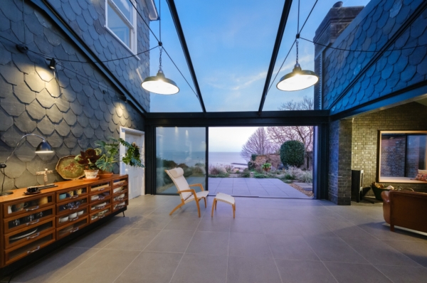 A tiled indoor living space featuring a glass roof, a lounge chair, and wide sliding doors to the patio.