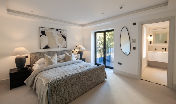 Modern bedroom with a textured grey bed, abstract wall art, glass balcony doors, and an attached bathroom.