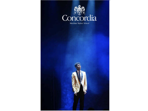 A young man in a gold jacket stands under a blue spotlight beneath a "Concordia" logo.