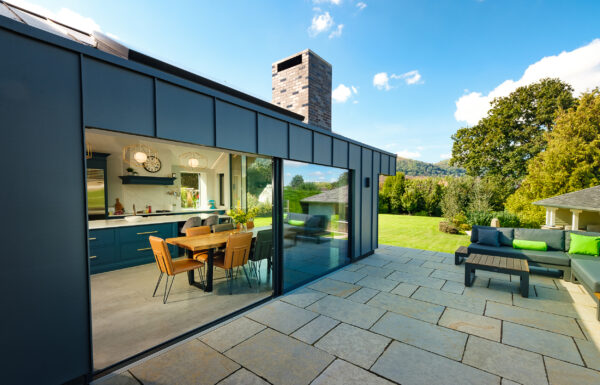 Modern kitchen-diner with massive open sliding glass doors leading out to a paved patio and lush garden.