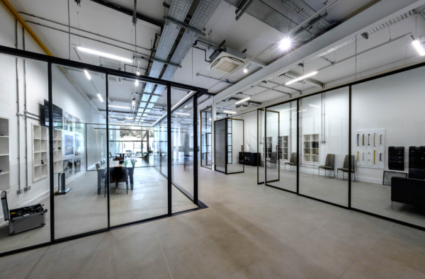 Open-plan showroom space divided by sleek black-framed glass partitions under industrial ceilings.