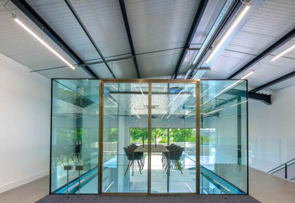 A glass-walled meeting room box elevated above a lower level, showcasing a long table and chairs.