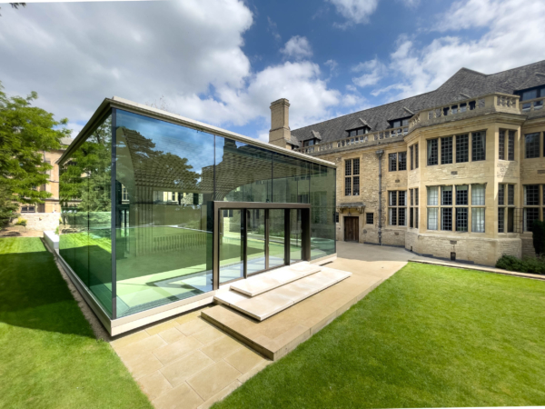 Rhodes House Oxford, A modern glass building addition beside a traditional stone mansion with a green lawn.