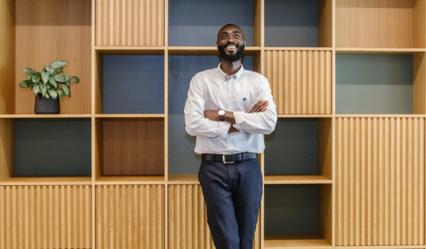 A smiling, bearded man stands with crossed arms in front of a modern wooden grid shelving unit.