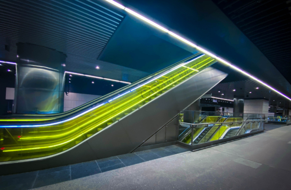 Underground station with a wide escalator and bright white lighting panels.