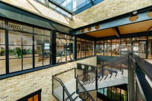 An indoor atrium view showcasing a multi-level office with glass walls, brick facades, and mesh staircases.